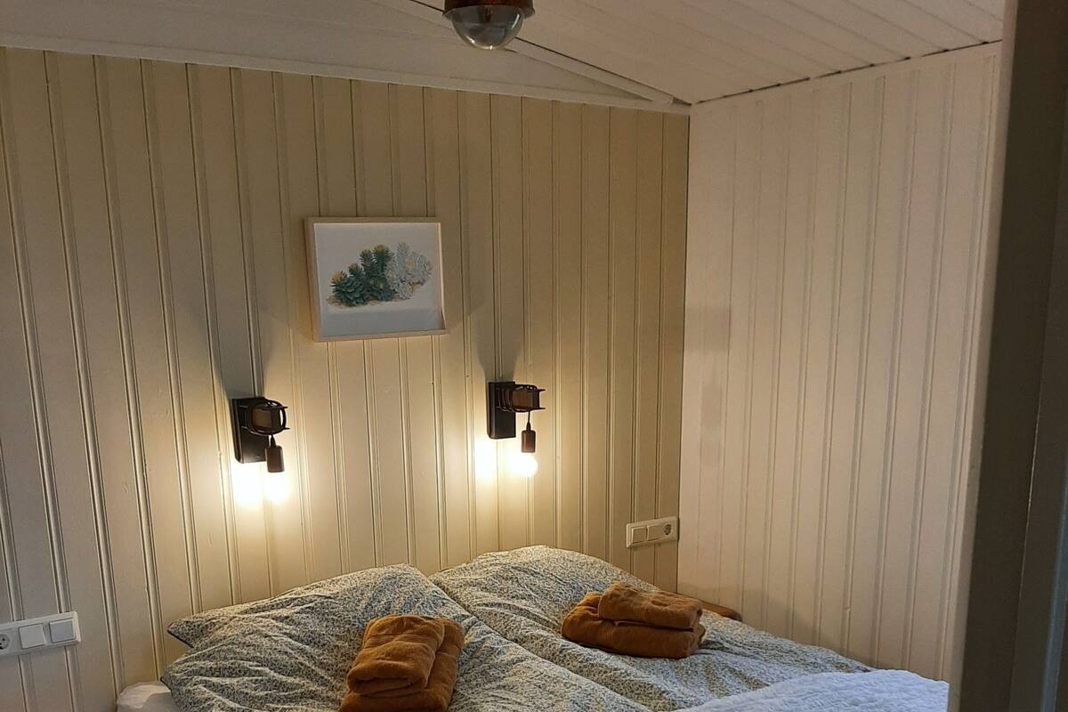 Un dormitorio con cama, dos lámparas de pared, una mesita de noche y suelo de madera.