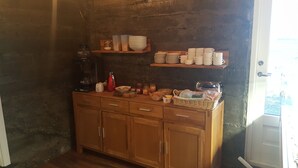 Een houten buffetopstelling met planken waarop kommen, borden en bekers staan, en een koffiezetapparaat op het aanrecht.