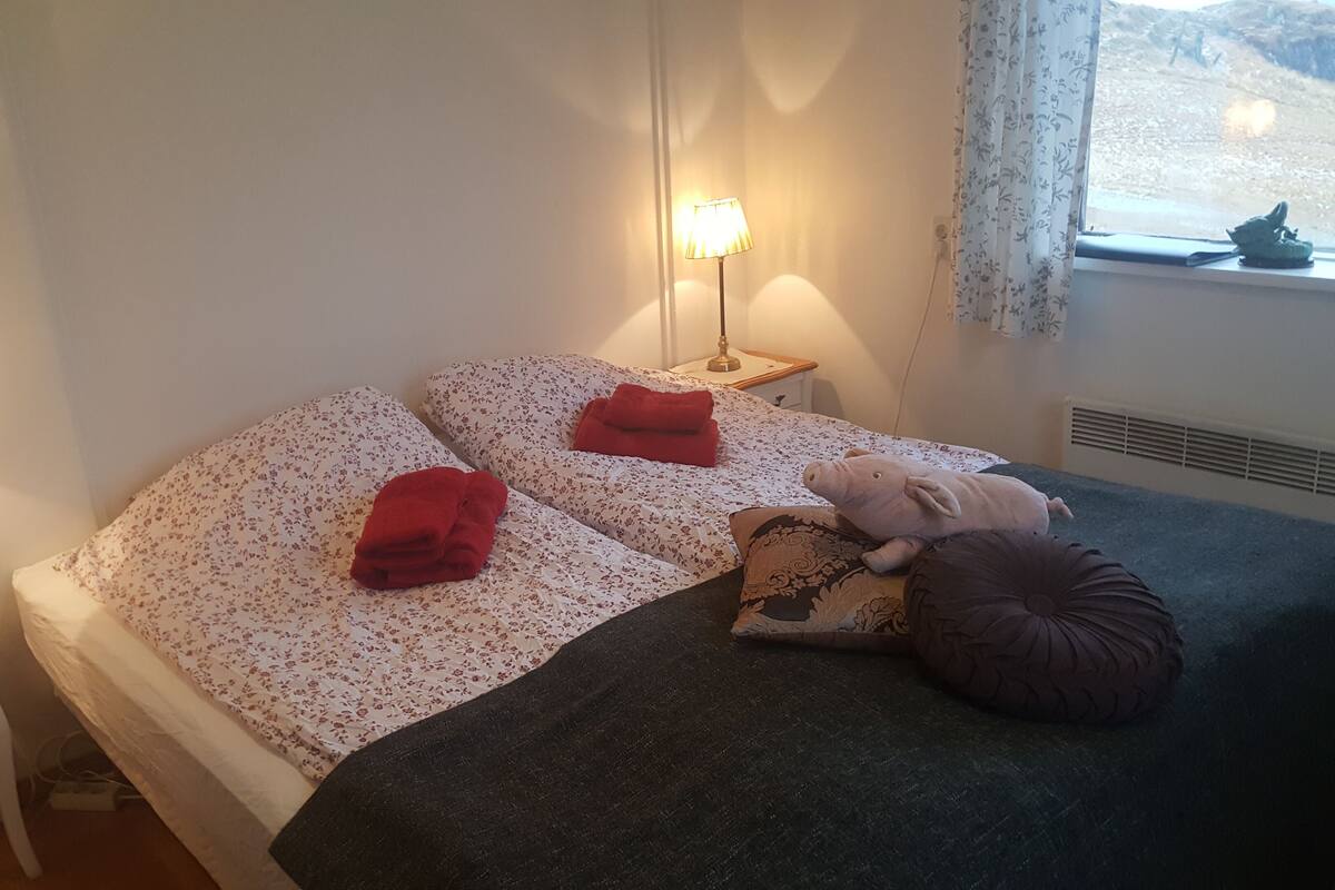 Un dormitorio con cama, dos lámparas de noche, un ventanal con vistas y una mesita de noche con lámpara.