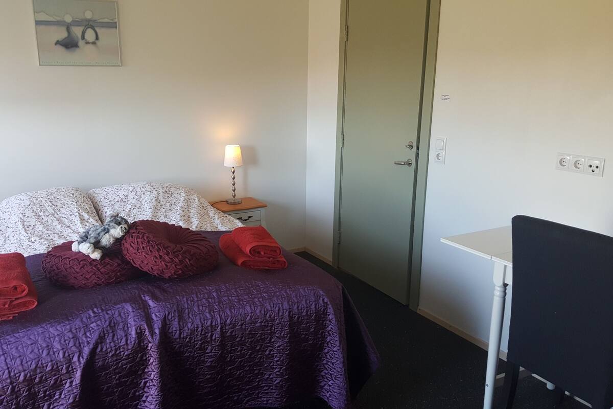 Habitación de hotel con cama, escritorio y silla. Hay toallas en la cama y una lámpara en la mesita de noche.