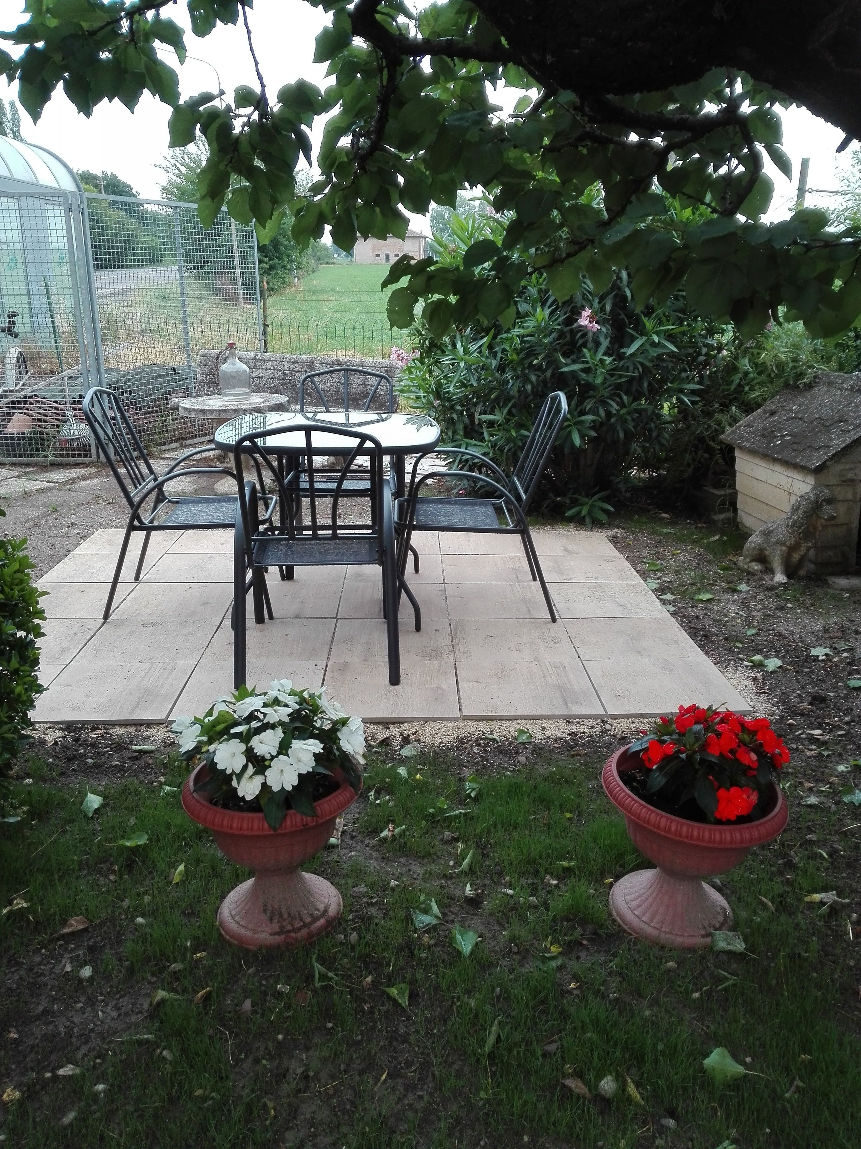 Eine Terrasse mit Tisch und Stühlen, umgeben von Topfpflanzen und einem eingezäunten Bereich.