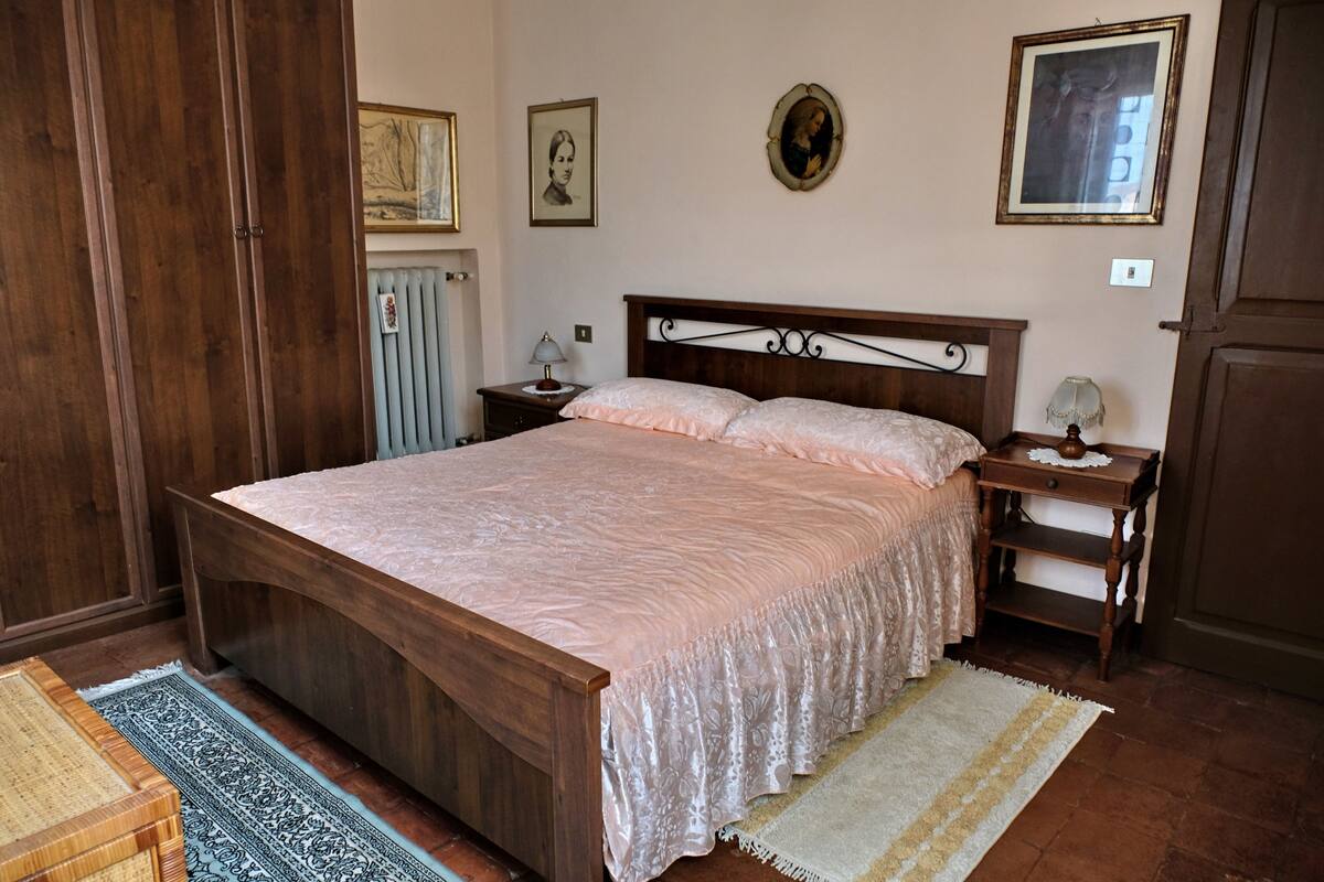 A bedroom with a wooden bed, two bedside tables, a nightstand, a radiator, and a wooden wardrobe.
