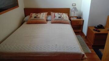Una cama bien hecha con almohadas estampadas, una mesita de noche con lámpara y una pequeña cómoda.
