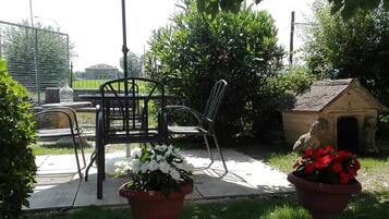 Un'area patio esterna con tavolo e sedie, una cuccetta per cani e due vasi di fiori.