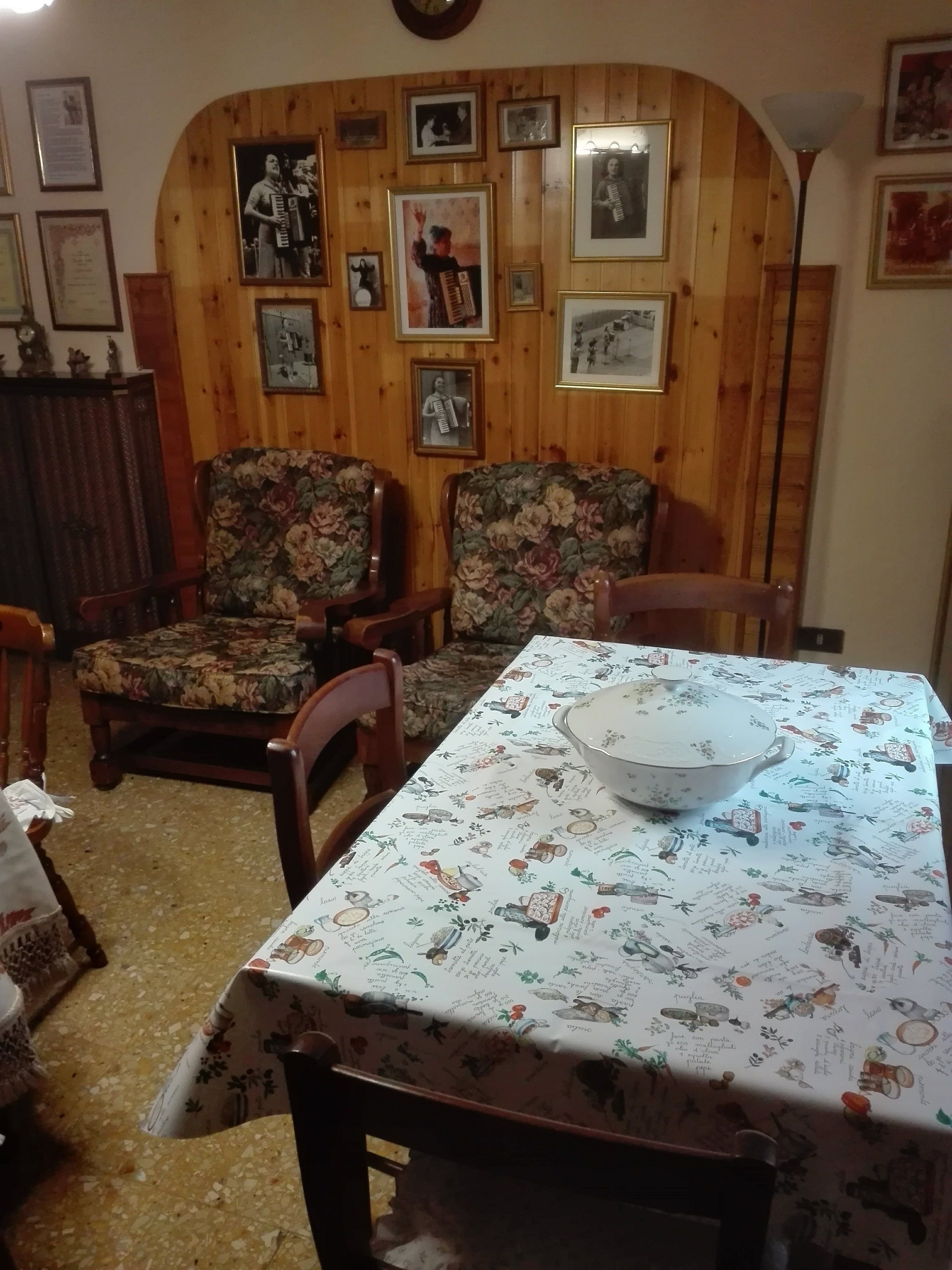 A dining area with a table set for two, wooden panel walls, and framed pictures on the wall.