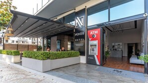 A modern hotel exterior with a covered outdoor seating area, an ATM, and a reception desk. - Nemesis Hotel (Sarandë)