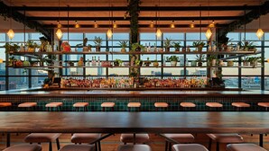 A bar with multiple shelves of bottles, a long counter, and several stools. - The Hoxton, Chicago (Chicago)