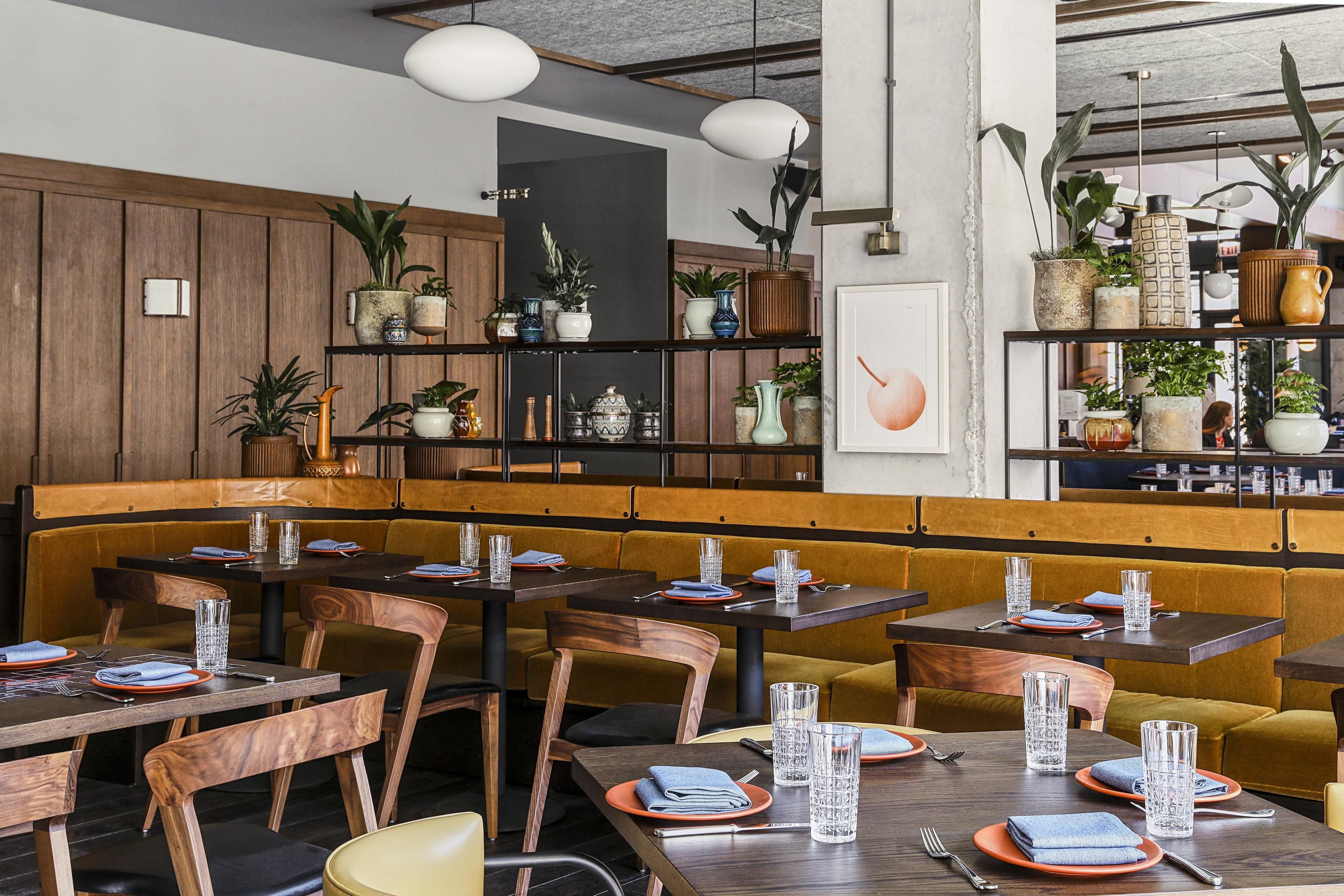 A restaurant with wooden booths, tables set with plates, glasses, and cutlery. There are shelves with potted plants and decorative items.