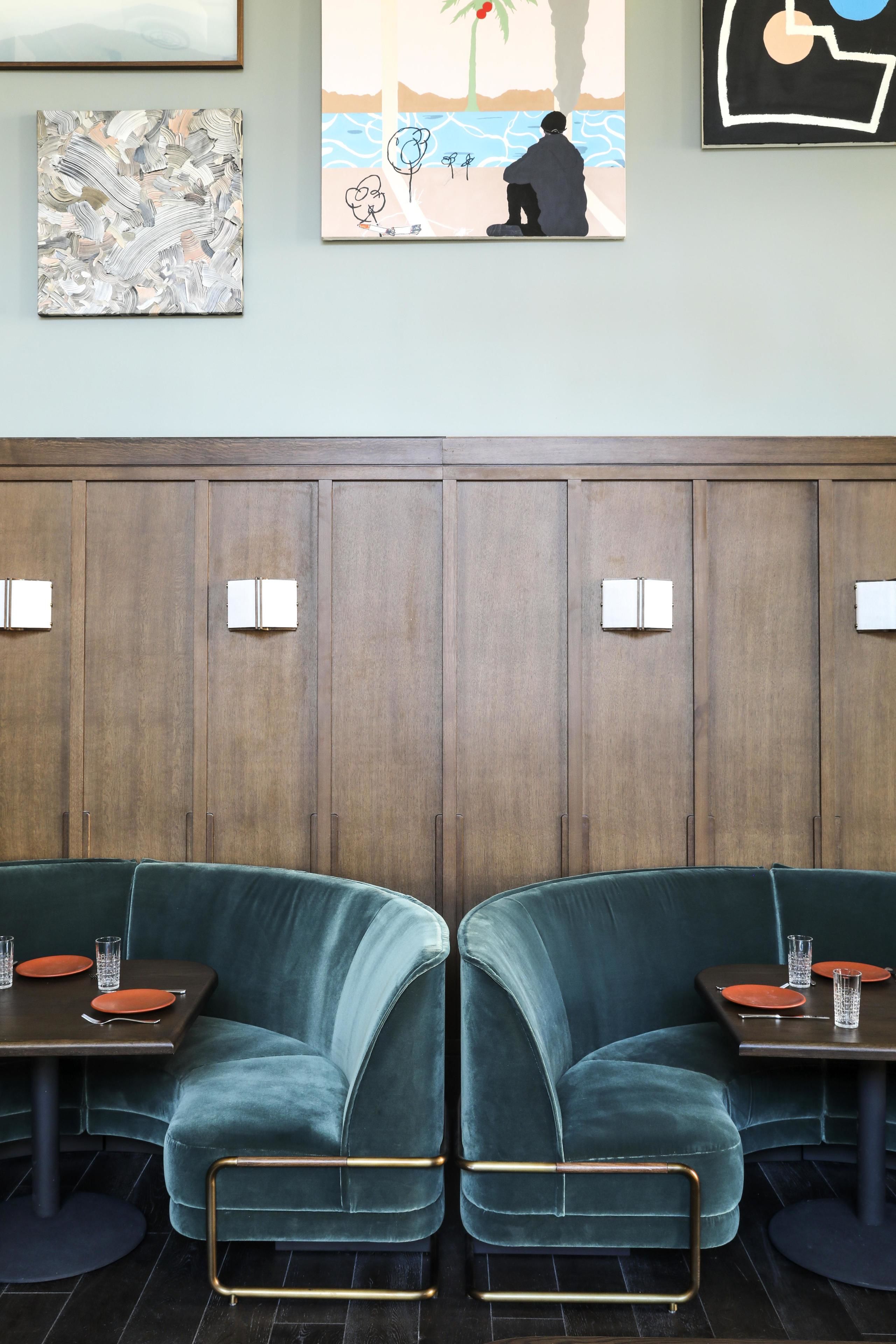 Un comedor moderno con dos sofás de terciopelo, paneles de madera y obras de arte en las paredes.