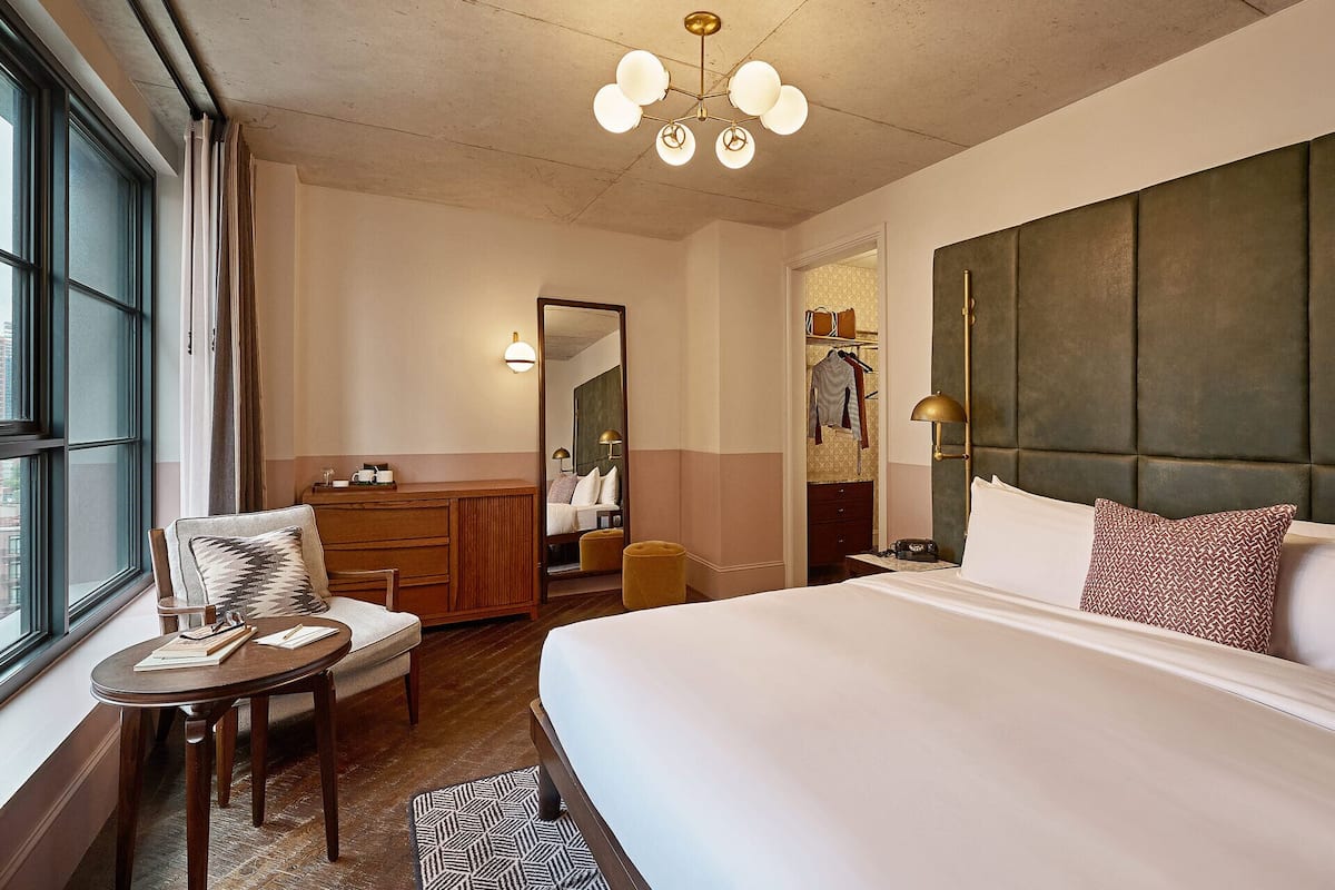 A hotel room with a large bed, a desk, a chair, a wardrobe, and a mirror.