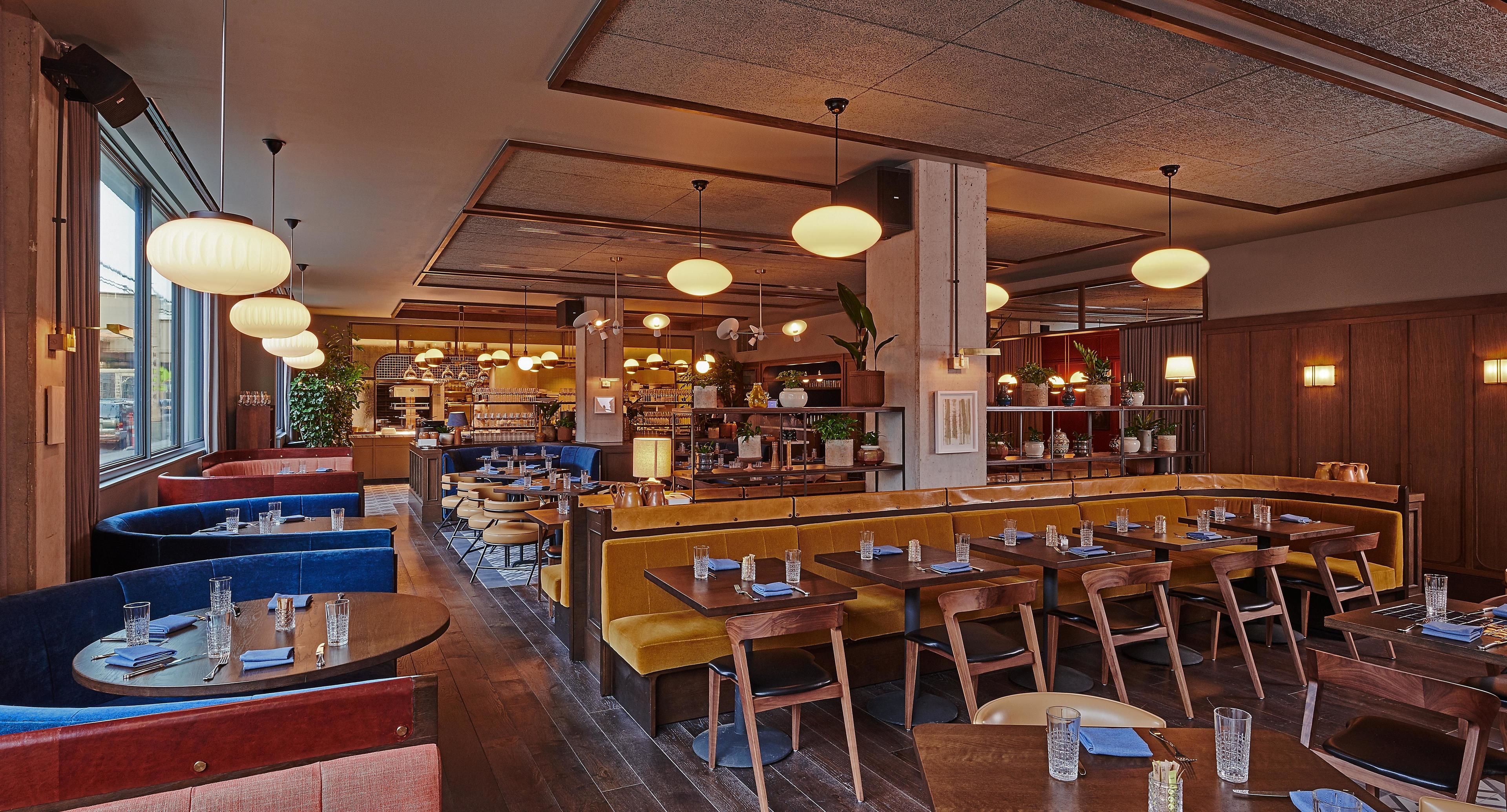 A restaurant with booths and tables, wooden floors, and hanging pendant lights.