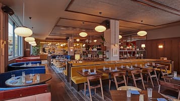 A restaurant with booths and tables, wooden floors, and hanging pendant lights.