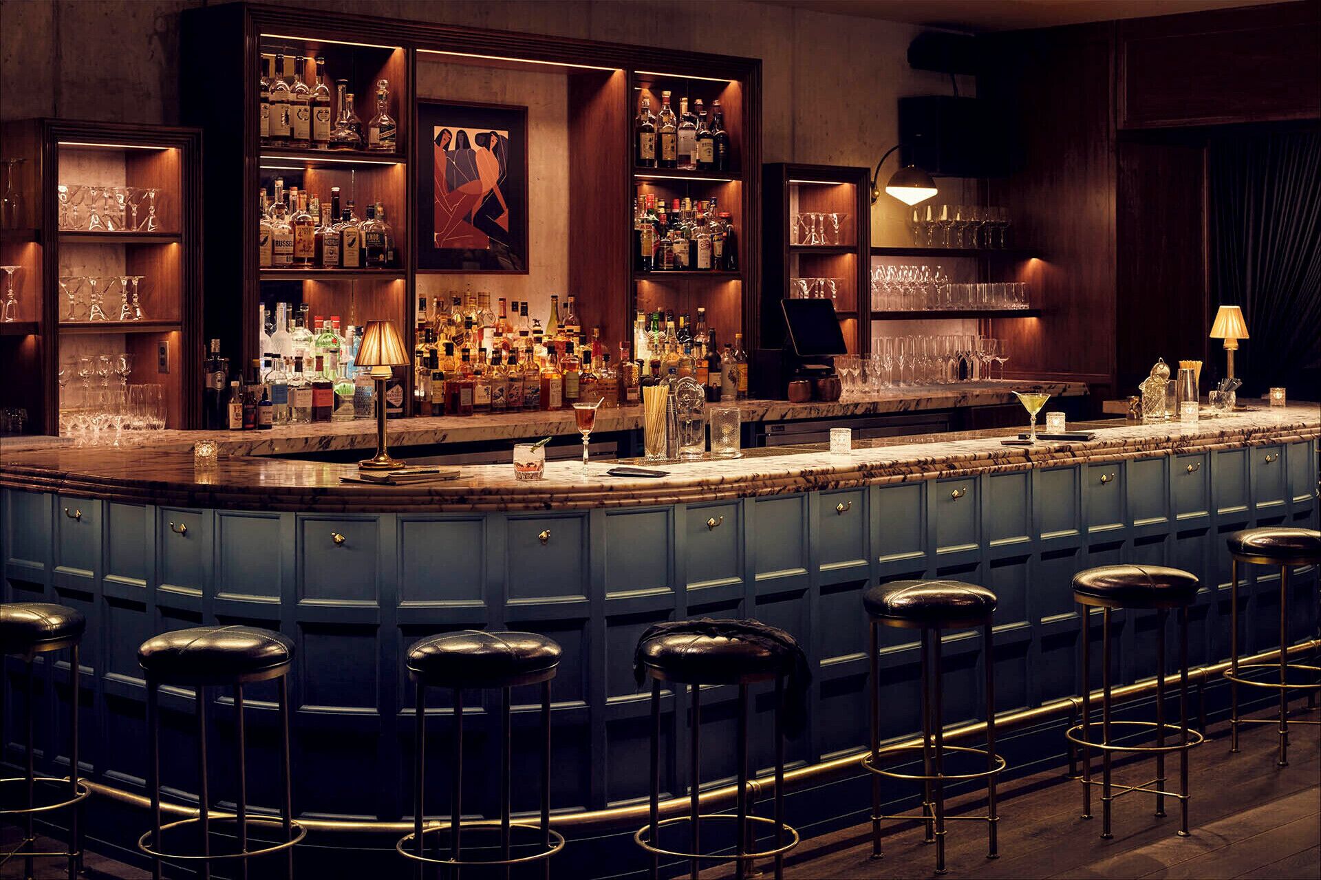 A bar area with a curved counter, multiple stools, and shelves stocked with bottles and glasses.