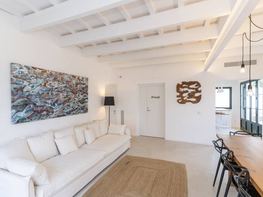 Una sala de estar moderna con un sofá blanco, un cuadro abstracto grande, una mesa de comedor de madera con sillas y una puerta con la etiqueta "Privat".
