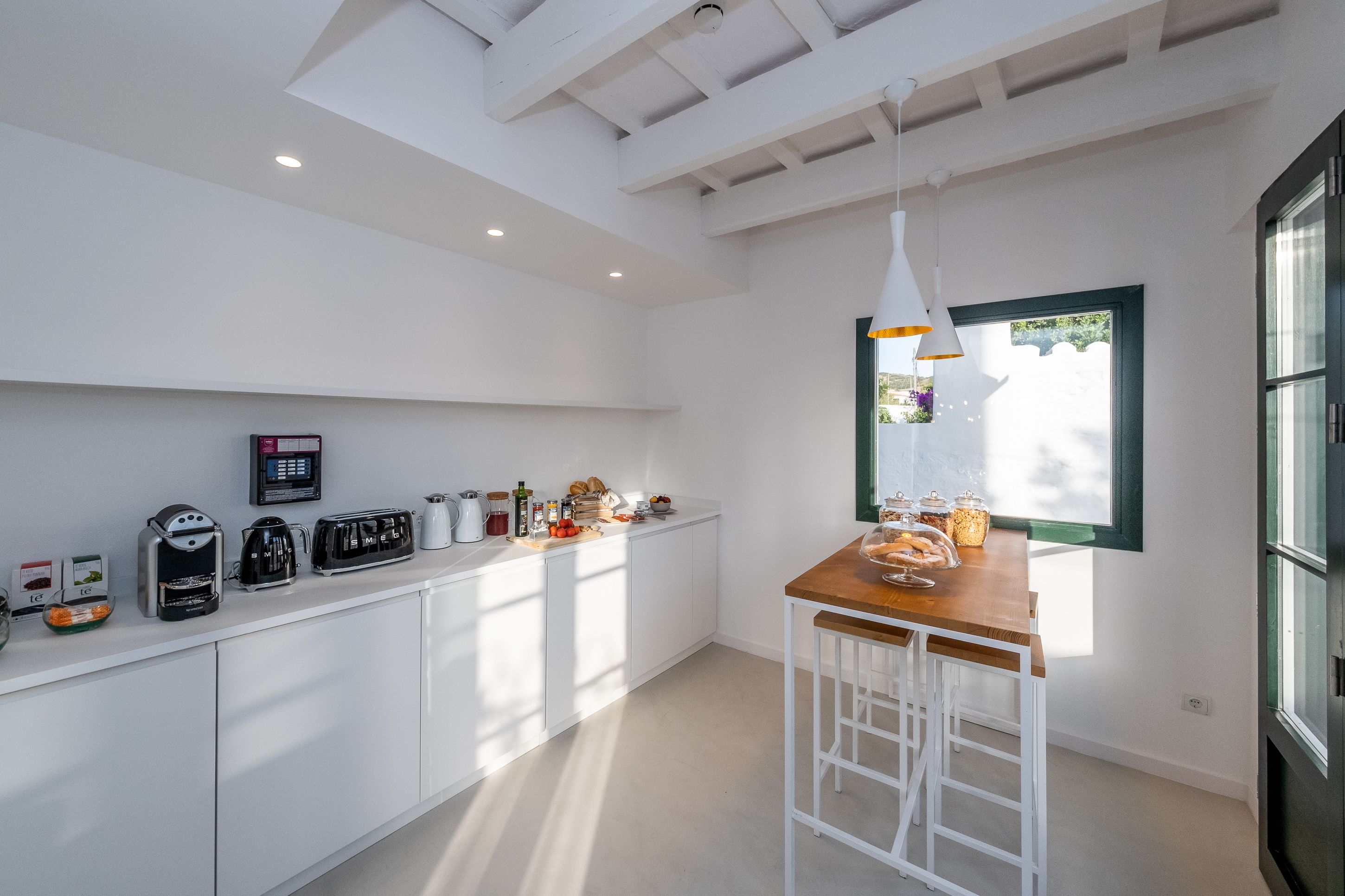 A modern kitchen with white cabinetry, a wooden bar counter, and a window providing natural light.