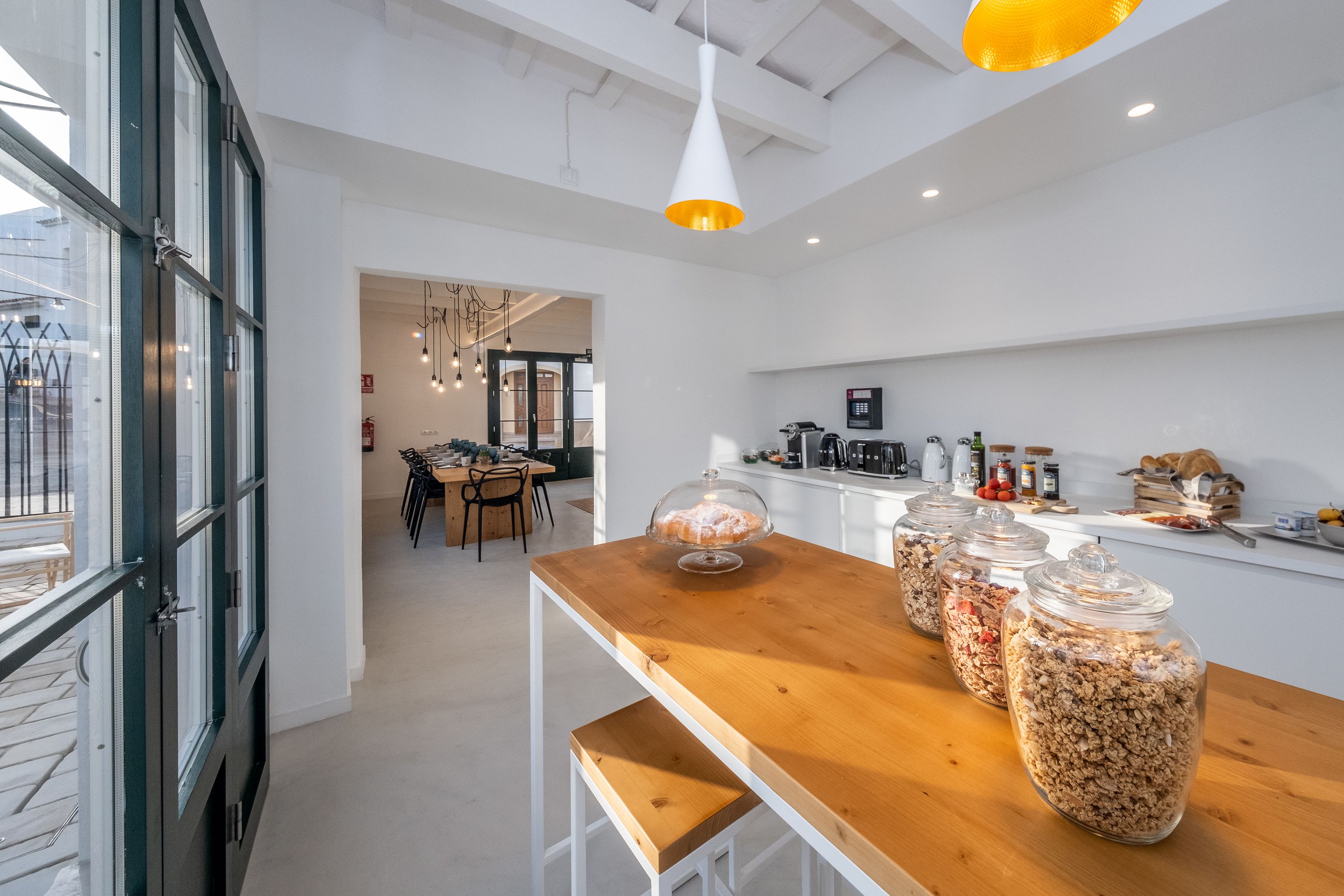 Une cuisine moderne avec un comptoir-bar en bois, des bocaux en verre remplis de granola et une vue sur l’espace repas.