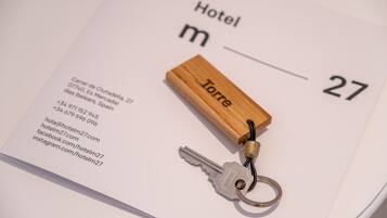 Un llavero de hotel con un bloque de madera con la etiqueta "Torre" y una llave, sobre una tarjeta de acceso a la habitación de hotel que muestra información de contacto y el número "27".
