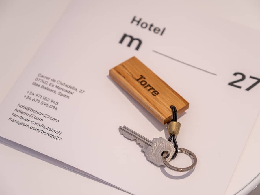 Un llavero de hotel con un bloque de madera con la etiqueta "Torre" y una llave, sobre una tarjeta de acceso a la habitación de hotel que muestra información de contacto y el número "27".
