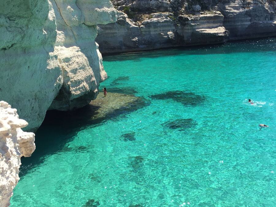 Ein klares türkisblaues Meer mit schroffen Klippen und spärlicher Vegetation.