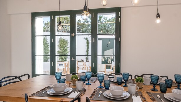 Un coin repas avec une table en bois dressée pour six personnes, de la verrerie bleue et des chaises noires.