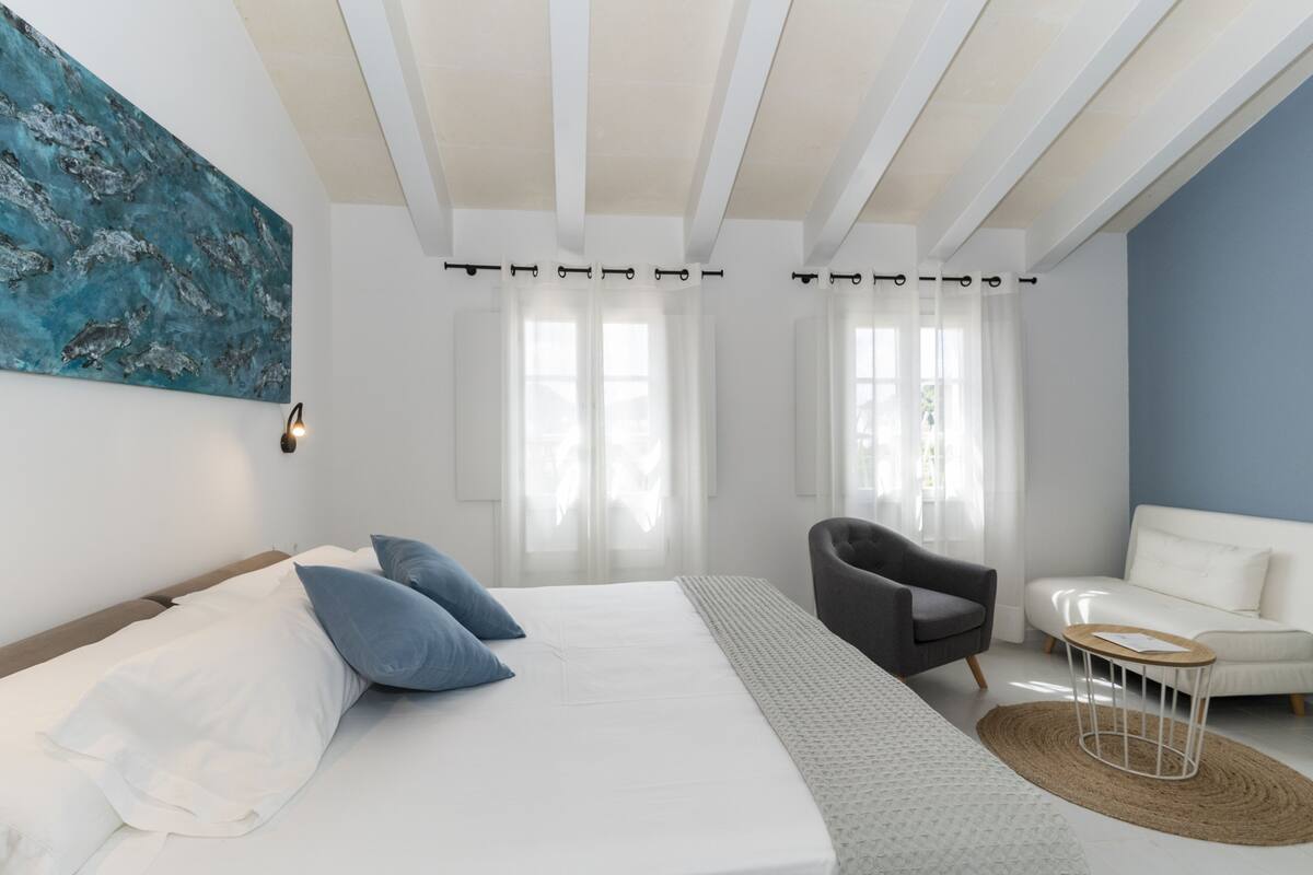 A modern bedroom with a bed, a chair, a sofa, and a large abstract painting on the wall.