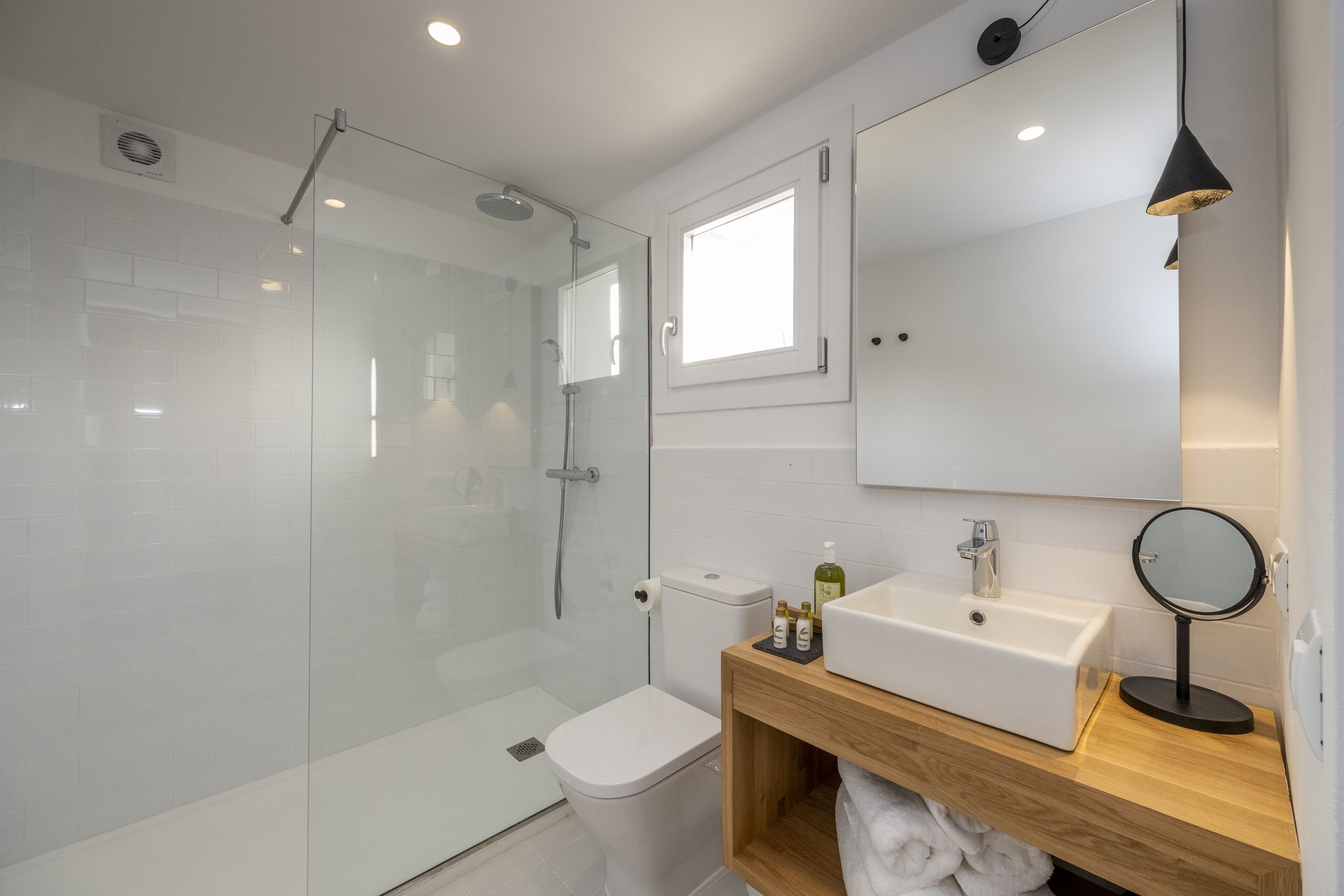 Un baño moderno con cabina de ducha de vidrio, inodoro blanco, tocador de madera con lavamanos y espejo.