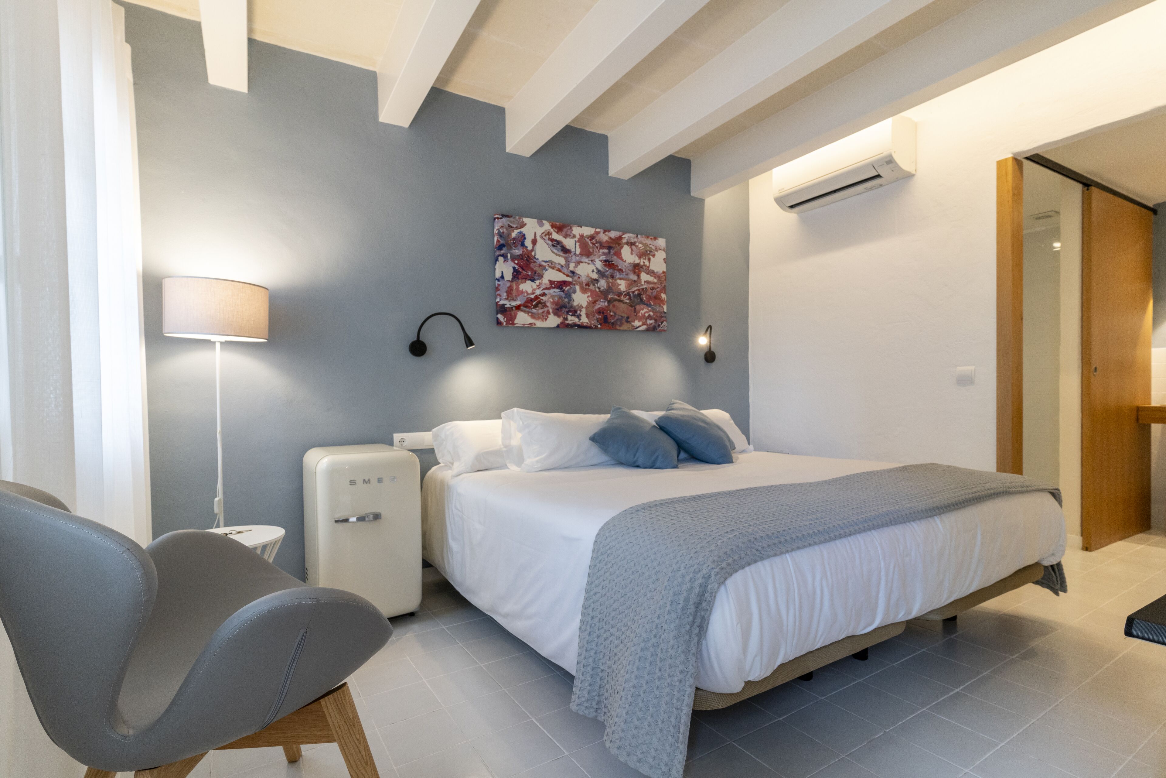 Een moderne slaapkamer met een bed, nachtkastje, lamp en een wandairconditioner.