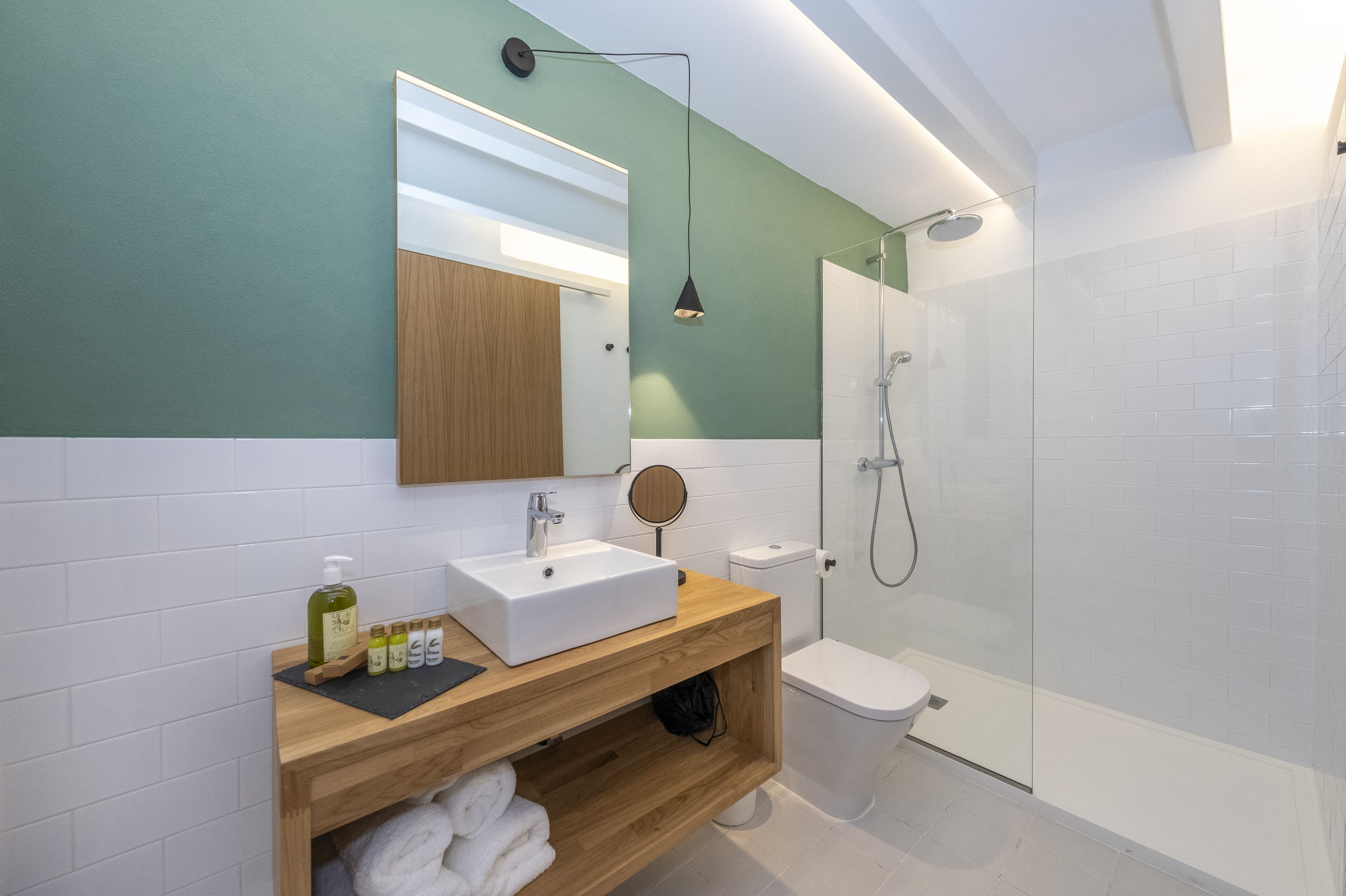 Un baño moderno con tocador de madera, lavabo blanco y ducha con mampara de vidrio.