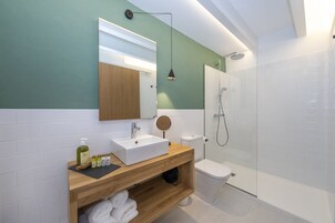 Un baño moderno con tocador de madera, lavabo blanco y ducha con mampara de vidrio.