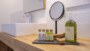 Un tocador de baño con lavamanos blanco, un espejo y una botella de aceite de oliva.