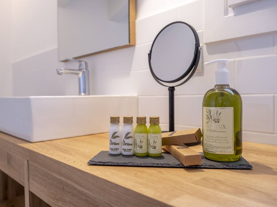 Un tocador de baño con lavamanos blanco, un espejo y una botella de aceite de oliva.