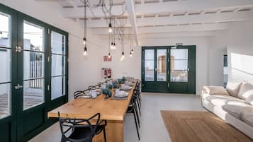 Un comedor con una mesa de madera larga dispuesta para una comida, rodeada de sillas, con un sofá y una alfombra al frente.