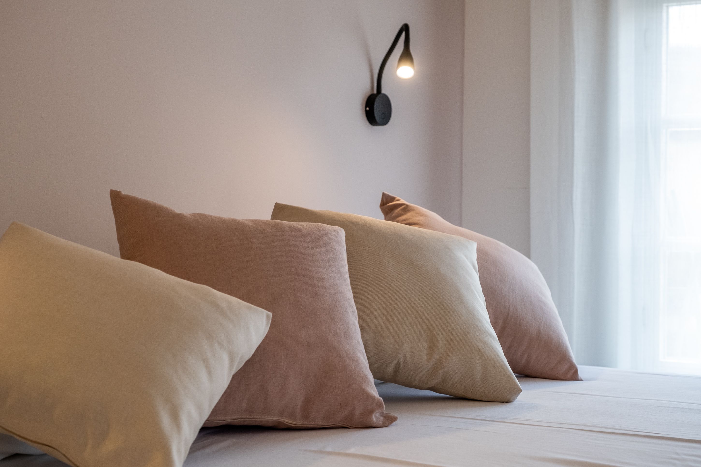 Un lit bien fait, agrémenté de plusieurs oreillers et d’une lampe fixée au mur.
