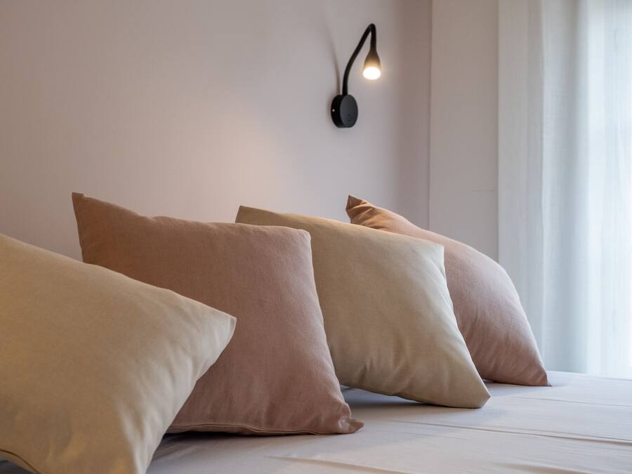 A neatly made bed with multiple pillows and a wall-mounted light fixture.