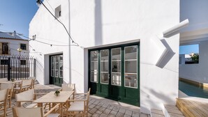 Un bâtiment blanc doté d’un patio carrelé, d’un espace extérieur aménagé pour s’asseoir et d’une piscine.