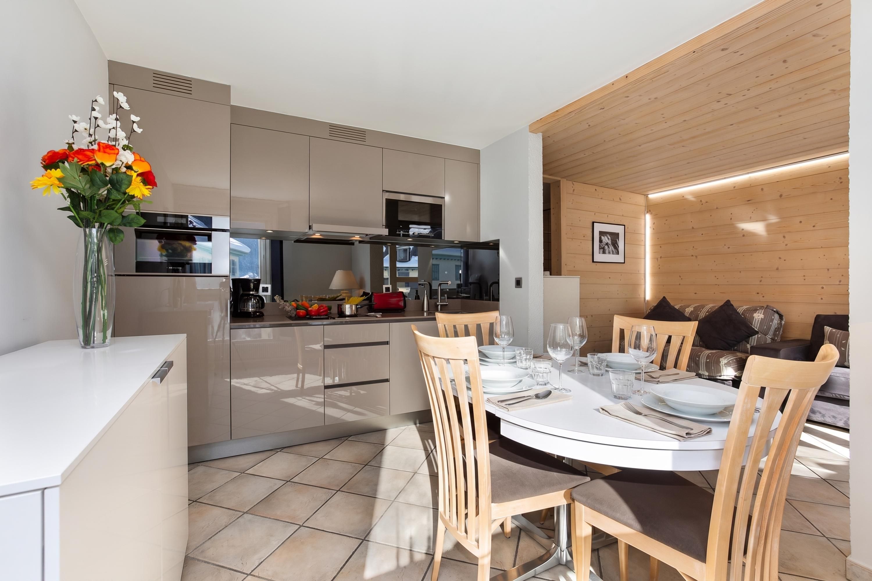 A modern kitchen with built-in appliances, a dining area with a round table, and wooden paneling on the walls.
