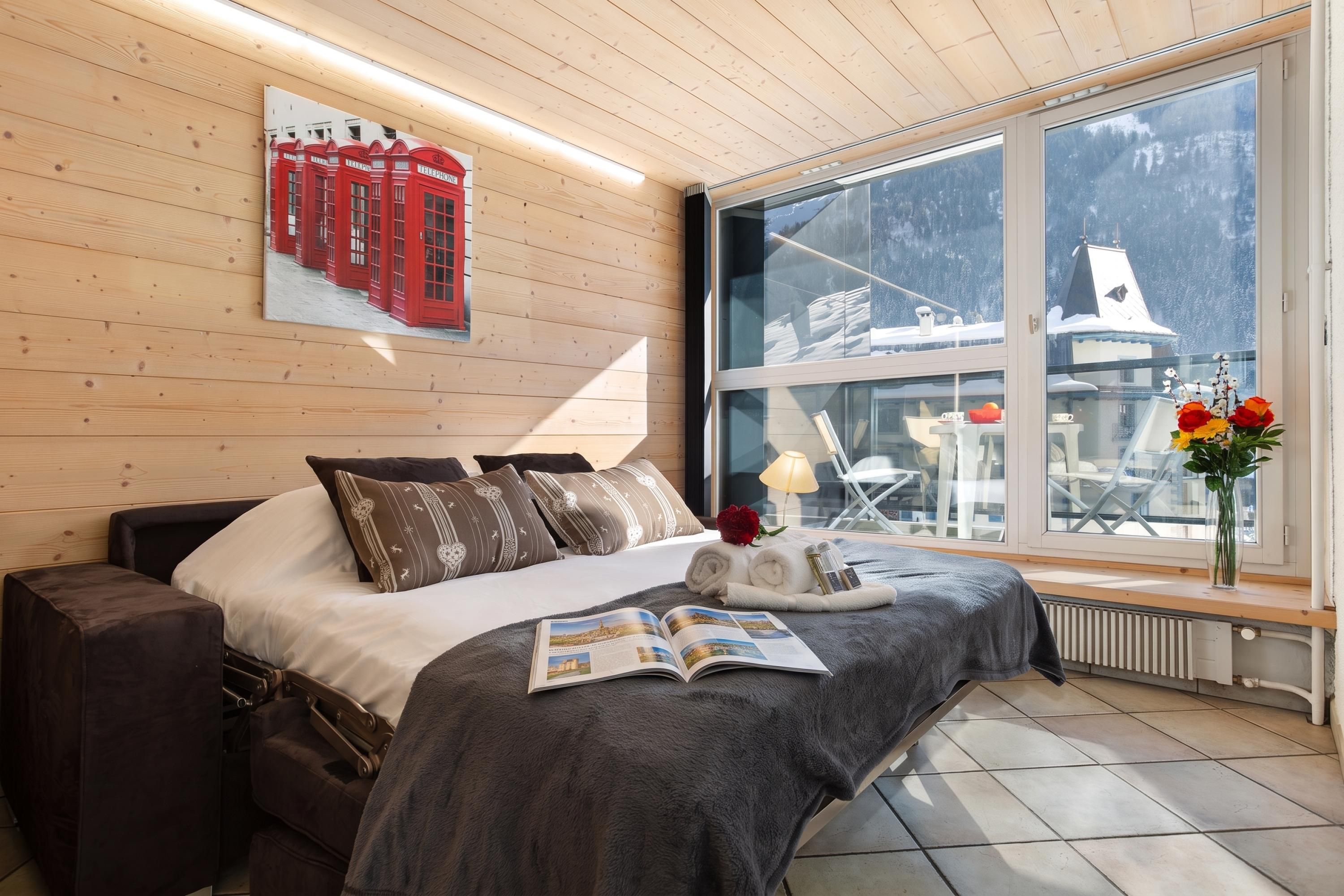 A bedroom with a bed, pillows, a magazine, and a window with a view of a snowy landscape.