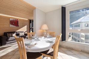 A dining area with a round table, chairs, and a view of a building through a window.