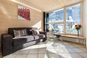 A modern living room with a wooden ceiling, a grey sofa with patterned cushions, a glass coffee table, and a large window with a view of a snowy landscape. - Apt L'Outa 209 Central Chamonix Mont Blanc view Parking, Chamonix, France (Chamonix)