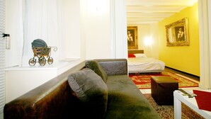 A room with a sofa, a small table, a red ottoman, a bed, and a painting on the wall. - Apartment Manufactura (Belgrade)