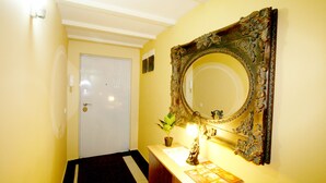 A hallway with a white door, a mirror with an ornate frame, a small potted plant, and a wooden vanity with a lamp. - Apartment Manufactura (Belgrade)