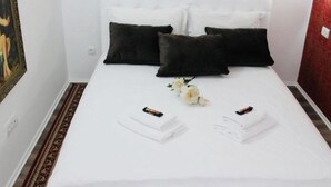 A neatly made bed with white linens, two black pillows, and a bouquet of white flowers. - Apartment Manufactura (Belgrade)