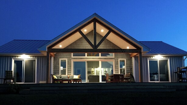 Une maison à deux étages dotée d’un porche abrité, de grandes portes-fenêtres coulissantes et d’un coin repas aménagé avec du mobilier d’extérieur.