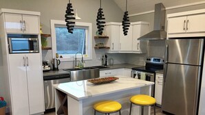 Une cuisine moderne avec des meubles blancs, des appareils en acier inoxydable et un îlot central doté de tabourets jaunes.