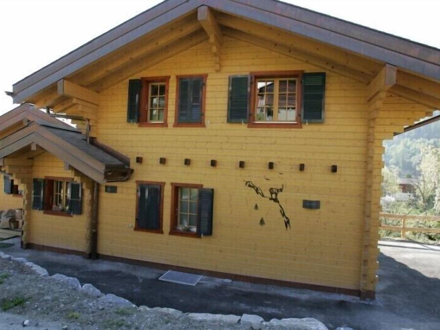 Una casa de madera de dos pisos con techo inclinado, varias ventanas con contraventanas y un pequeño balcón.