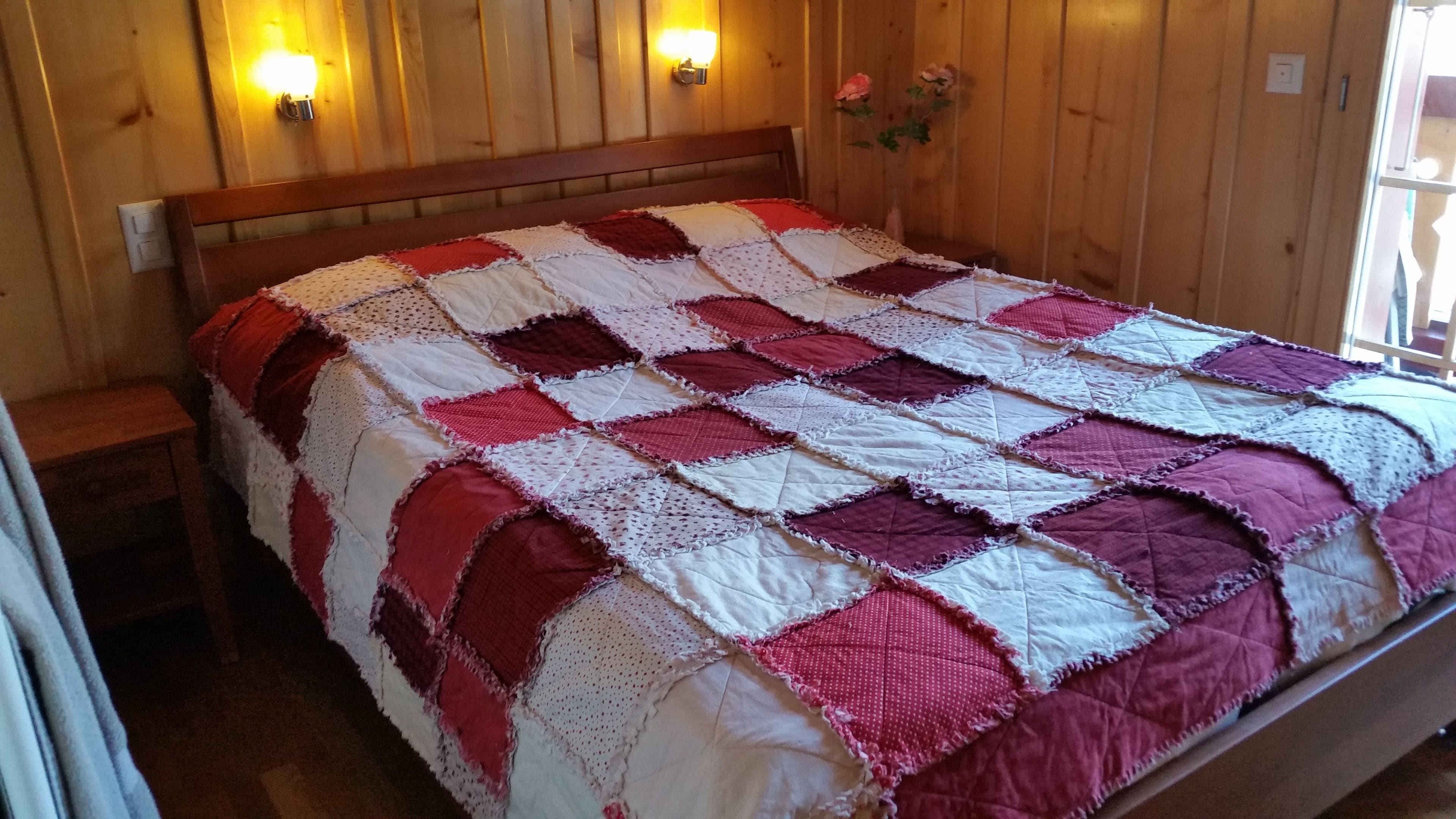 A wooden-paneled room with a bed featuring a red and white quilt.