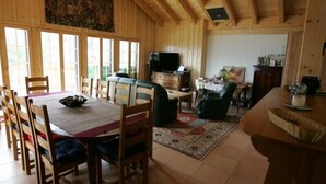 Um interior em madeira com mesa de jantar, cadeiras, sofá, televisão e cozinha.