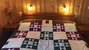 Quarto com painéis de madeira e uma cama com colcha de padrões geométricos.