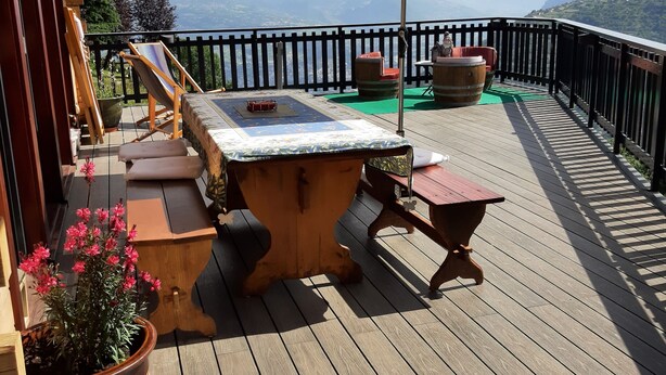 Um deck de madeira com banheira de hidromassagem, uma mesa e cadeiras, com vista para uma paisagem montanhosa.