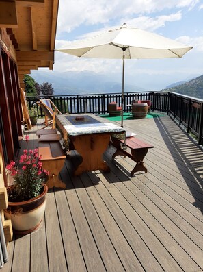 A wooden deck with a hot tub, a table, and chairs, overlooking a mountainous landscape. - Chalet la Rose des vents (Nendaz)